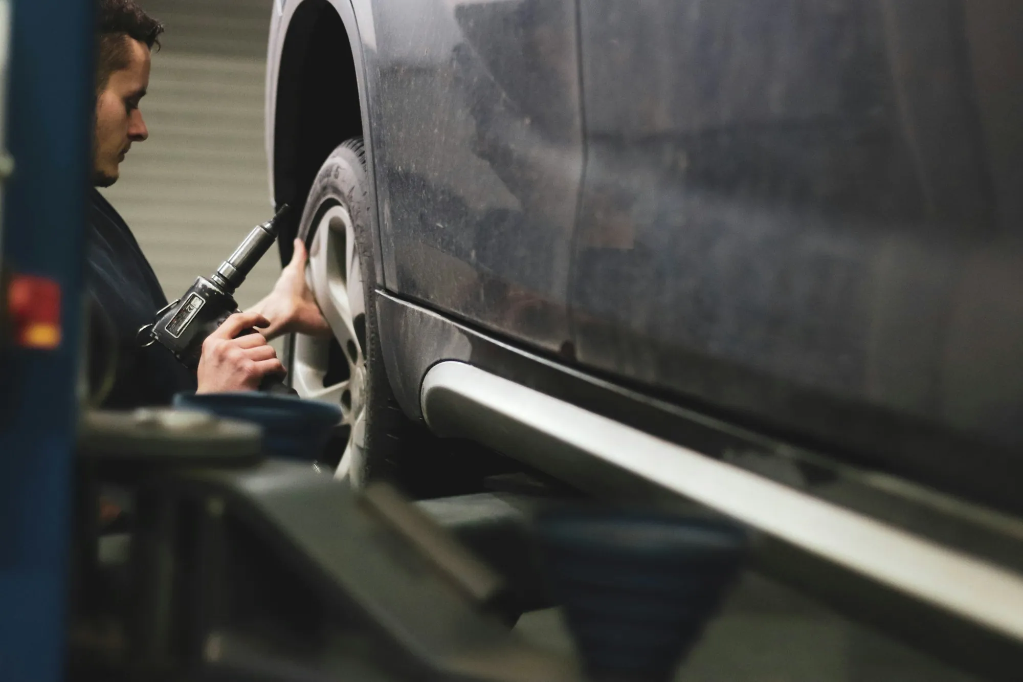Technician fitting a replacement front fender on a gray SUV in a repair bay