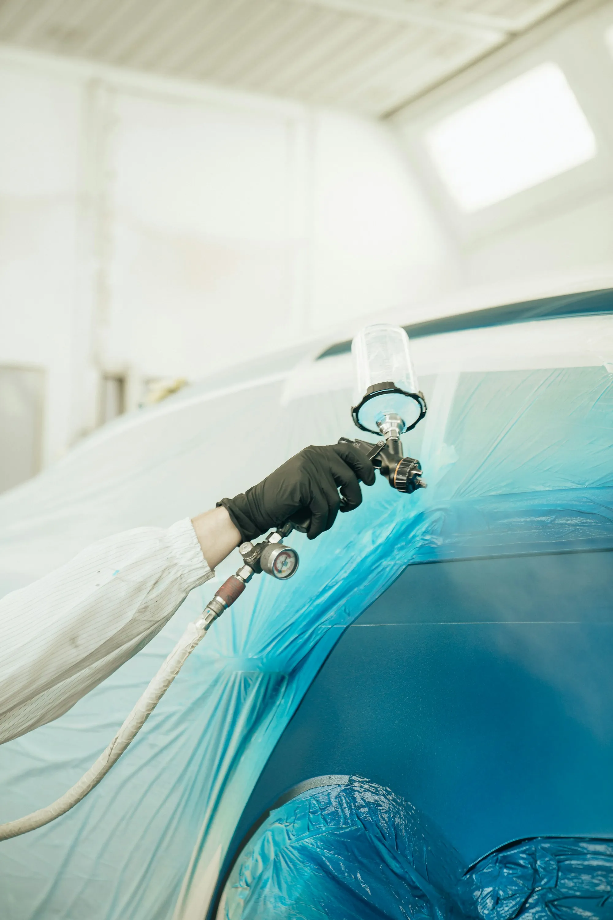 Body technician spraying paint on a car panel in a booth